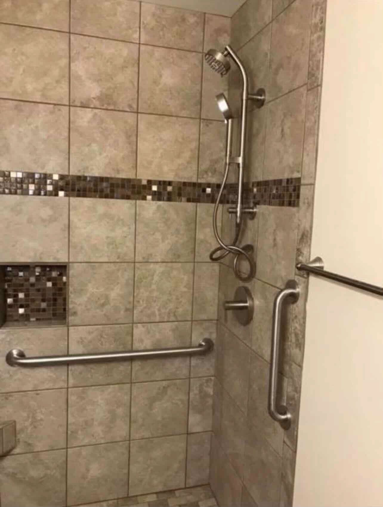A bathroom with a walk in shower and stainless steel handles.