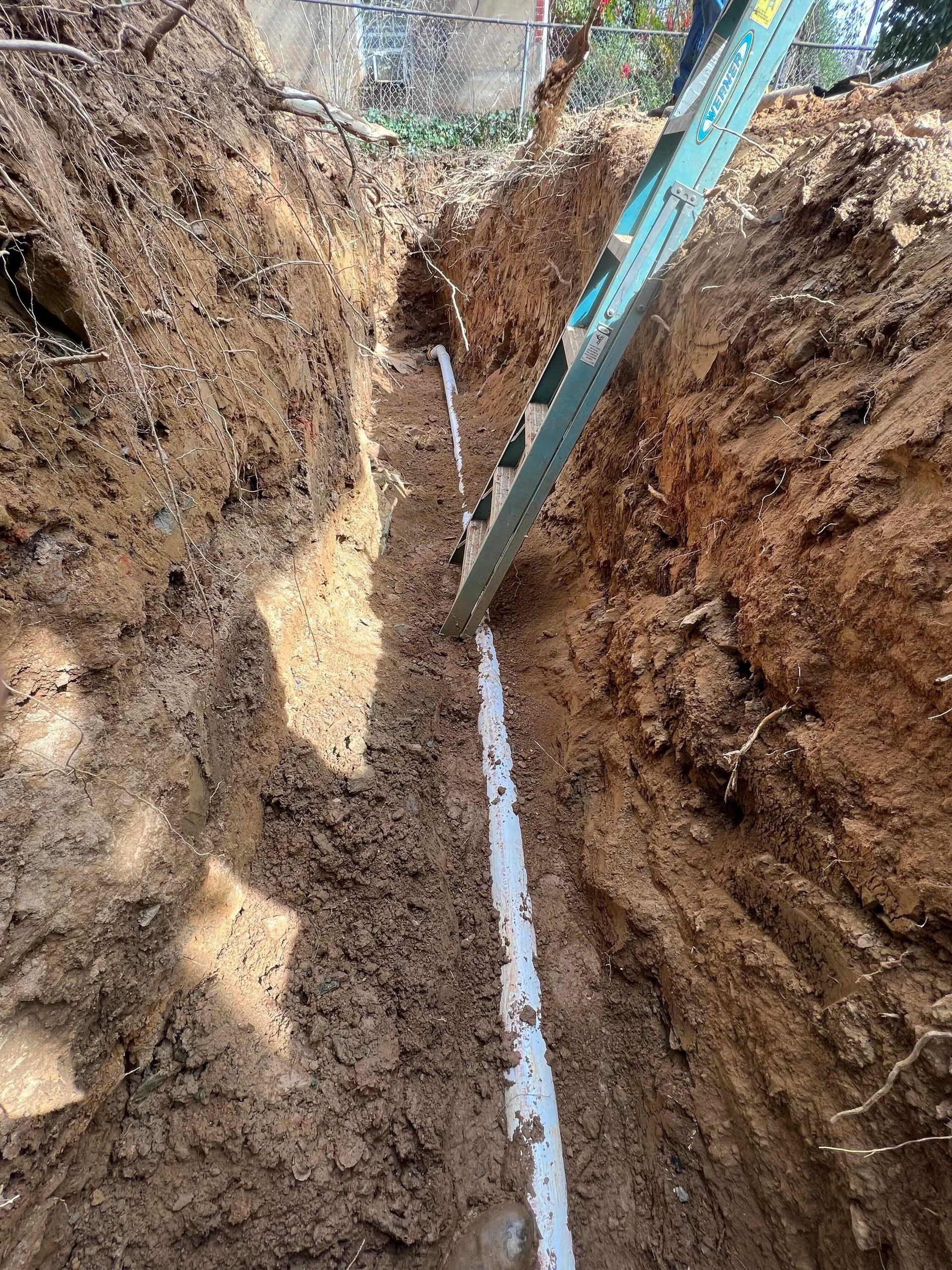A ladder is sitting in a trench next to a pipe.