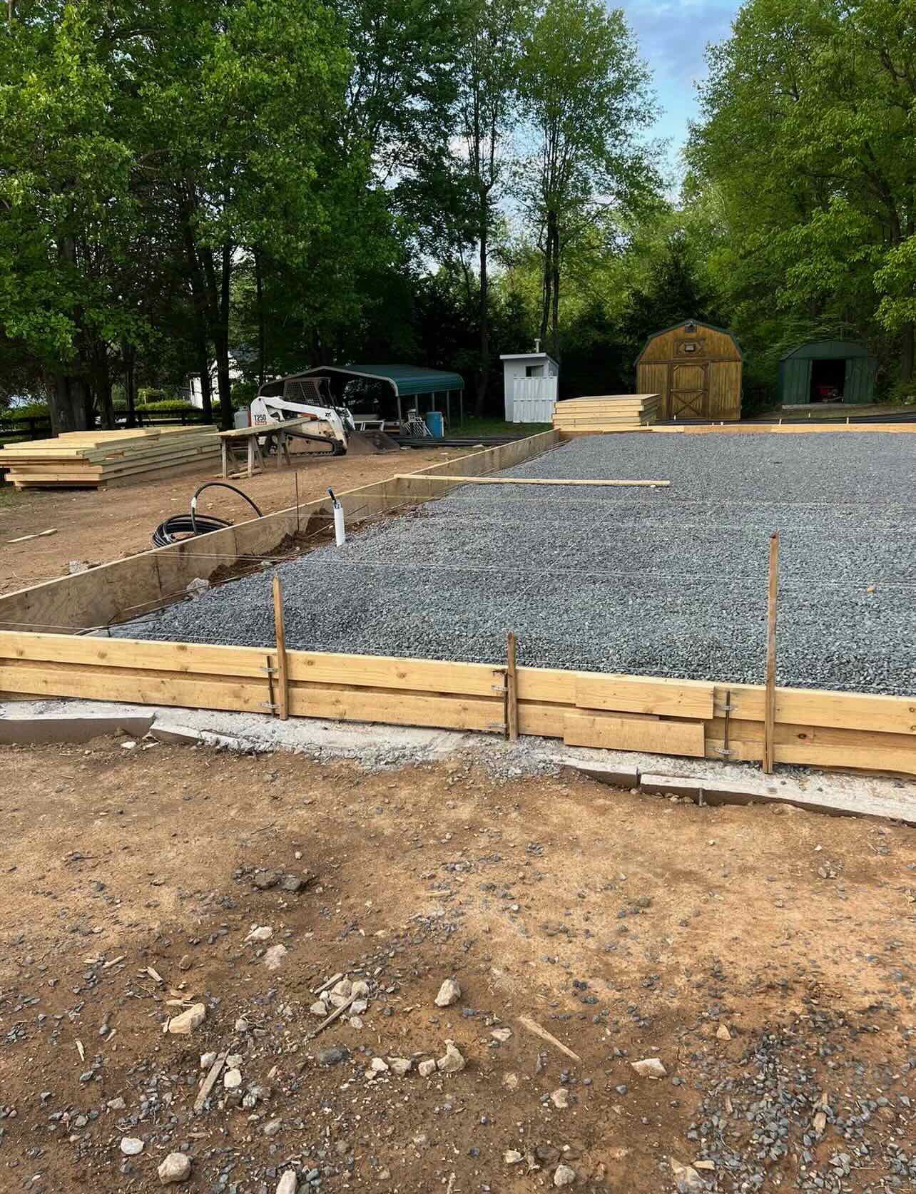 A wooden fence is surrounding a gravel area in a yard.