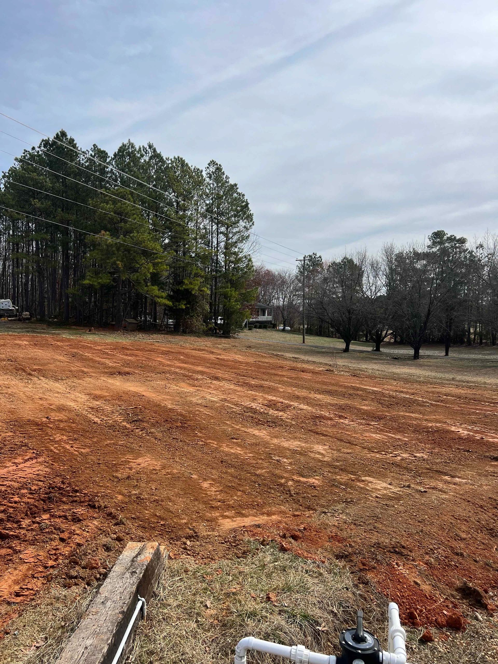 A large dirt field with trees in the background and a pipe in the foreground.