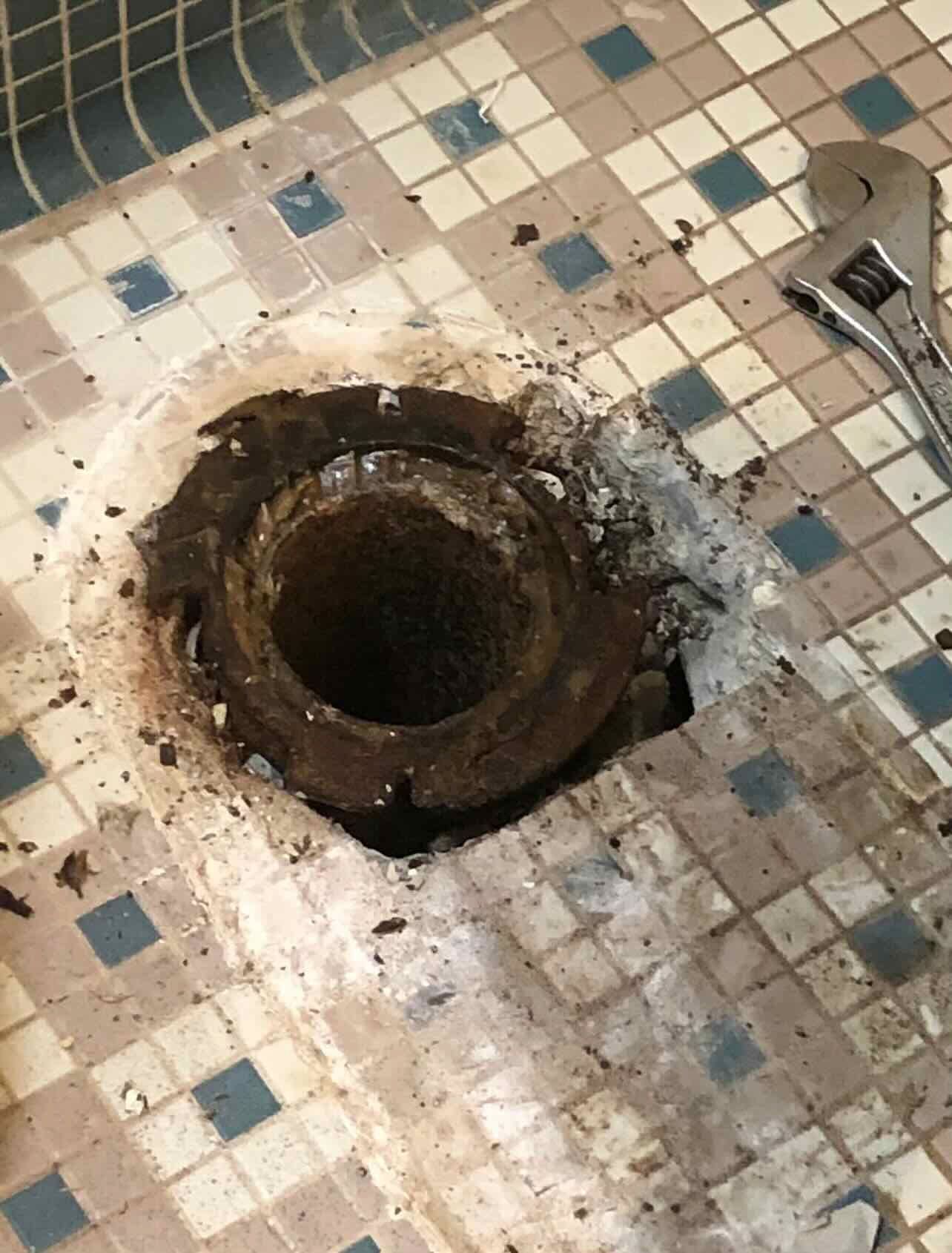 A wrench is sitting next to a hole in the floor