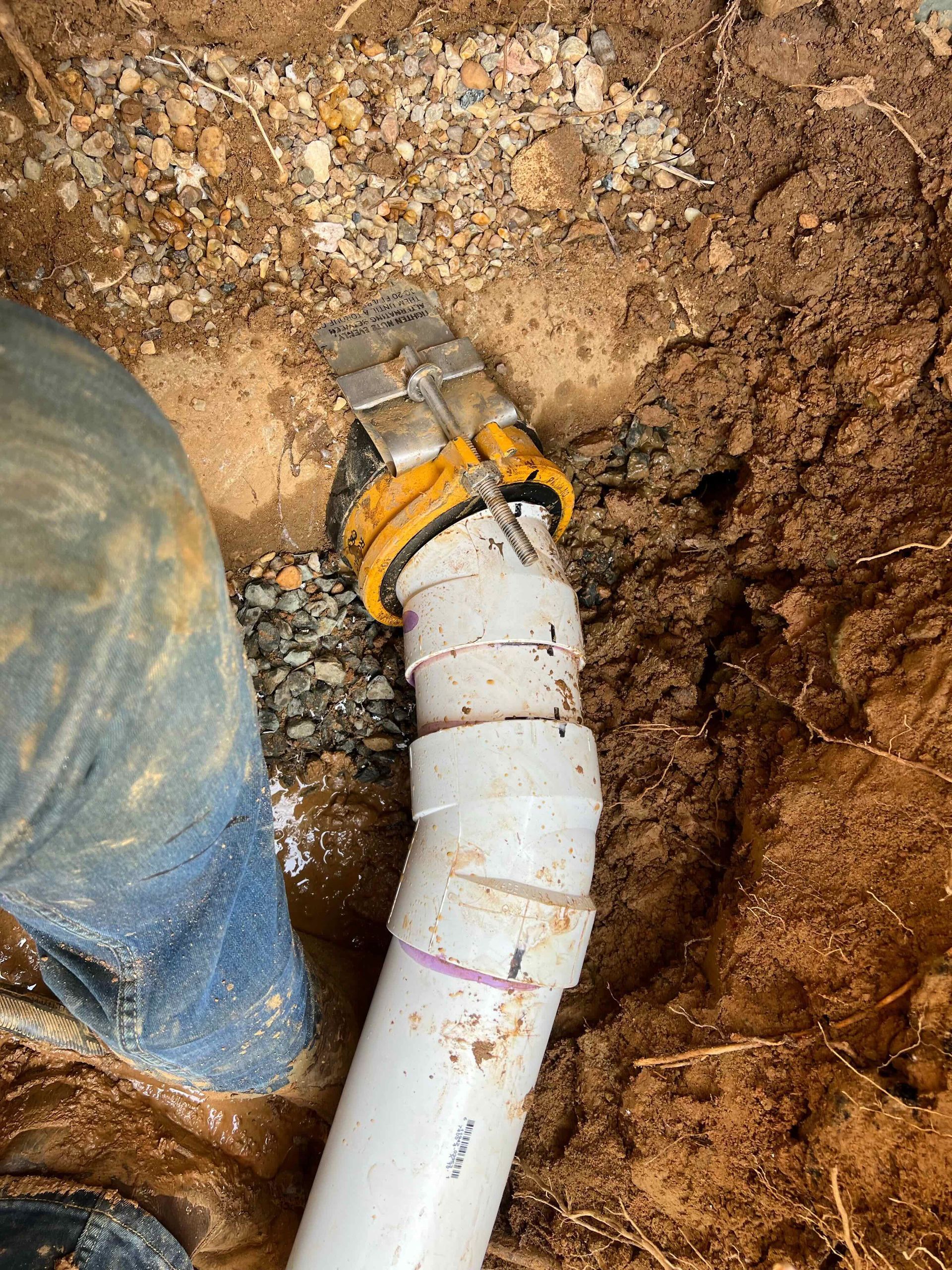 A person is working on a pipe in the dirt.