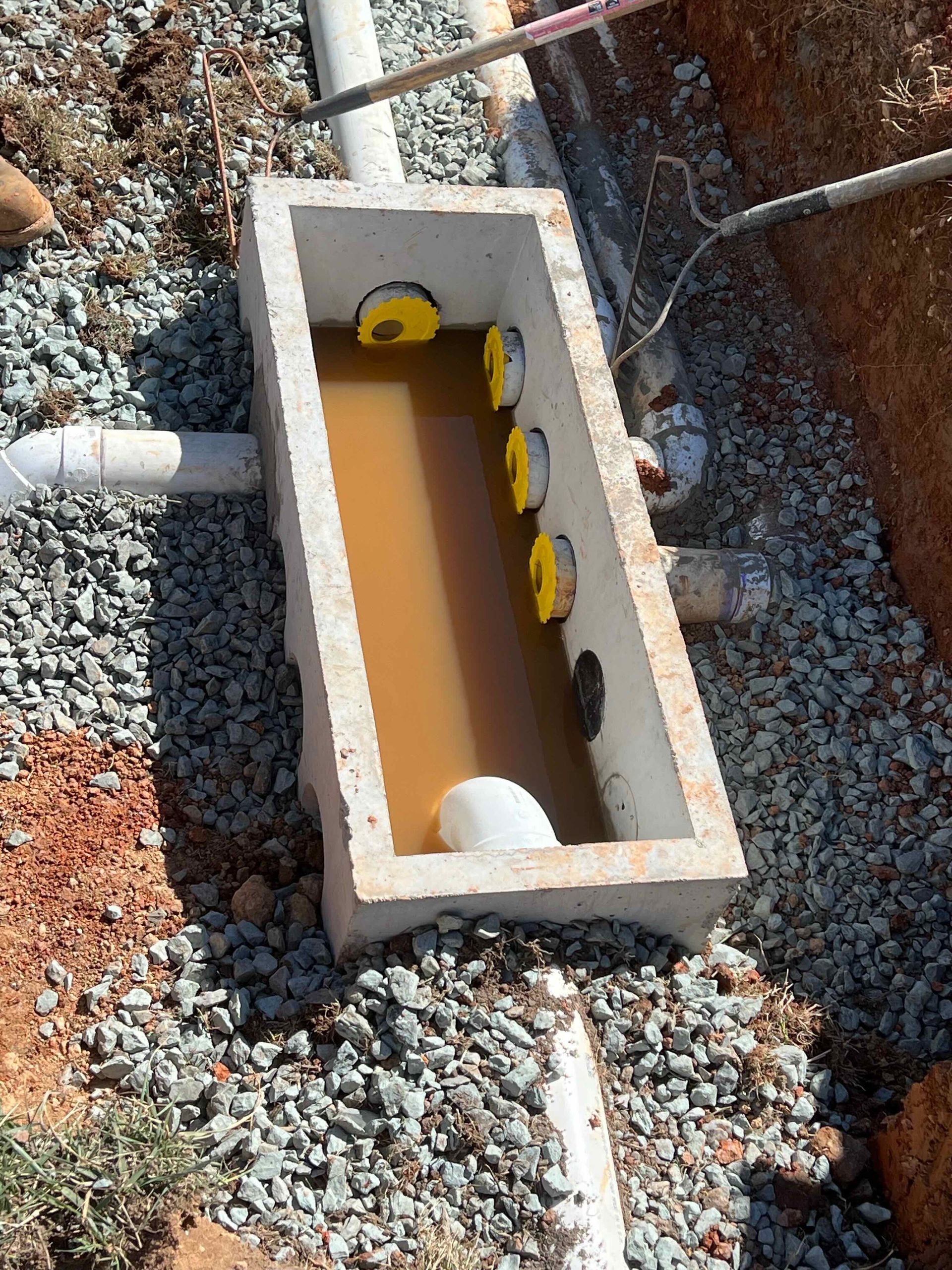 A concrete box filled with water and pipes in a gravel area
