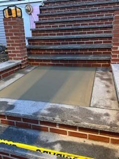 Brick steps leading up to a concrete landing with new, light gray concrete. Yellow caution tape in the foreground.