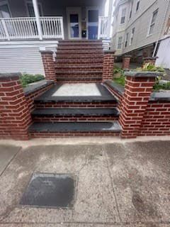 Brick stairs leading up to a building's entrance. The stairs are lined with brick walls and columns. Gray concrete sidewalk in front.