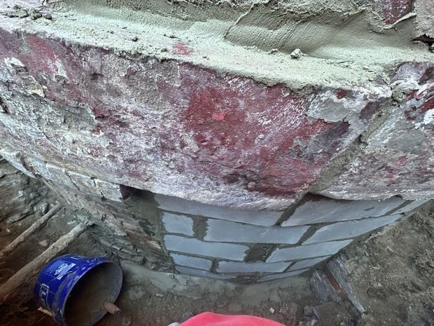 Close-up of a brick archway under construction, showing old red brick and new gray brick with mortar.