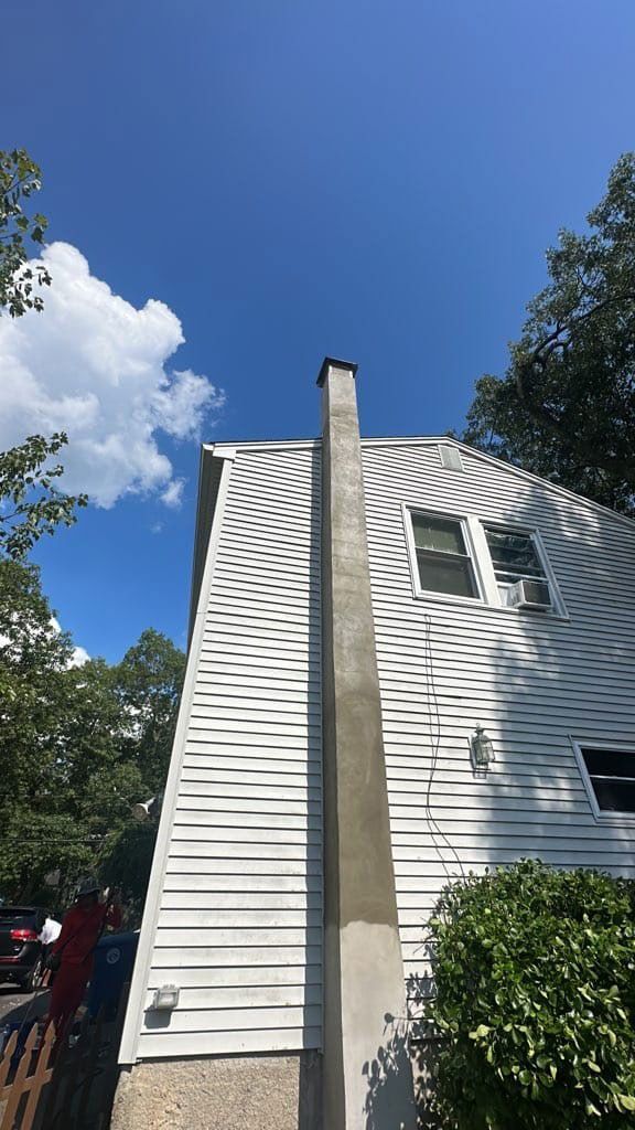 Chimney attached to a white house with blue sky and trees in the background.