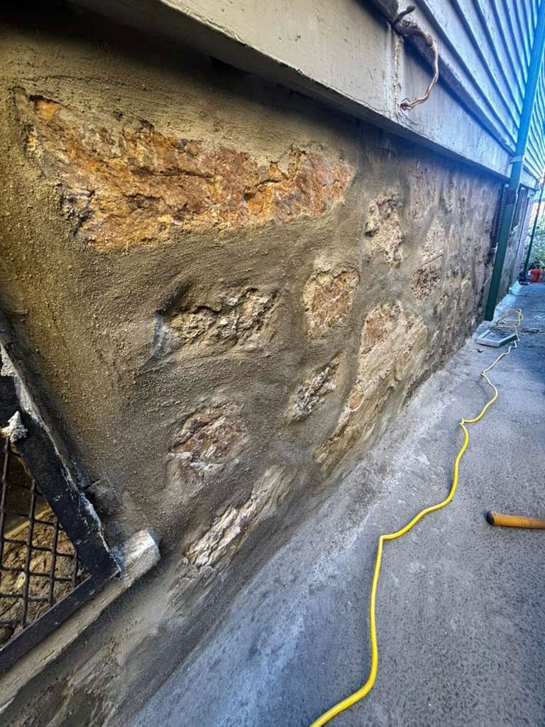 Stone foundation wall with concrete mortar; yellow power cord lies on the ground nearby.