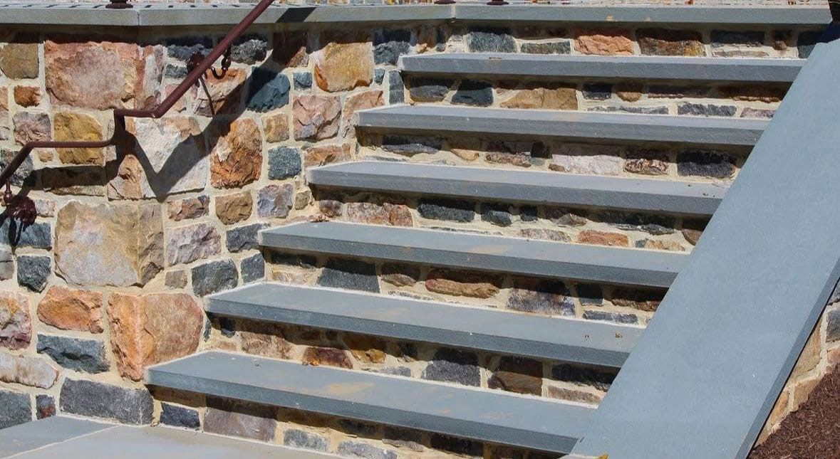 Stone steps with a stone wall and a rusty handrail.