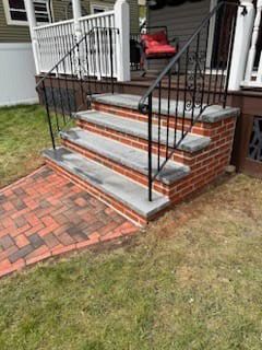 Brick and concrete steps leading to a porch, with black metal railings.