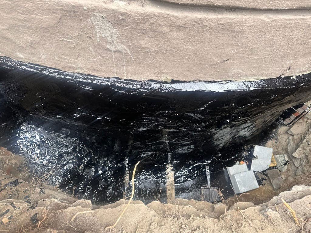 Dark, wet asphalt seals the inside corner of a brown, dirt-lined construction area.