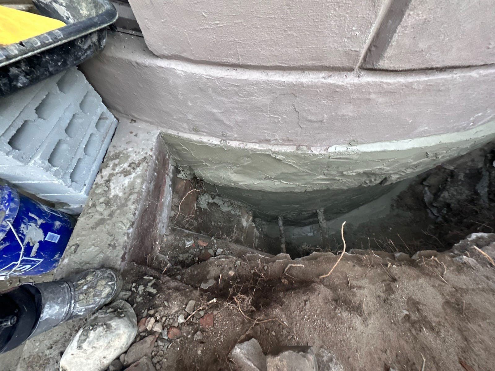 Close-up of a circular stone structure base with fresh cement. Construction materials are nearby, including cinder blocks and a bucket.