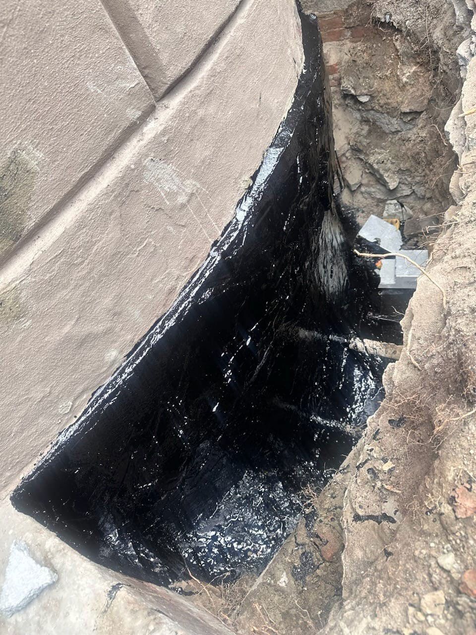 Dark tar lining a trench in the ground, next to dirt and a section of brick.