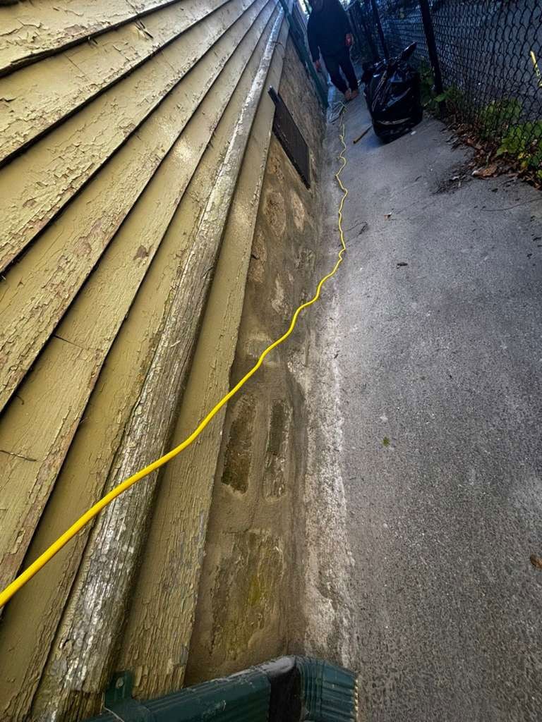 Yellow extension cord along a weathered building exterior and sidewalk. People in background.