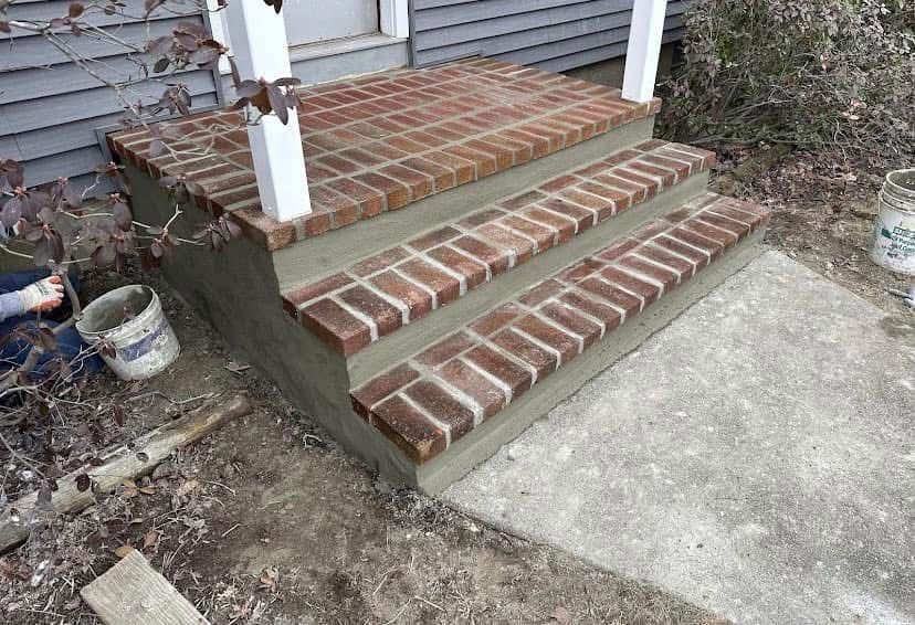 Brick steps leading up to a porch, with concrete and gray siding in the background.