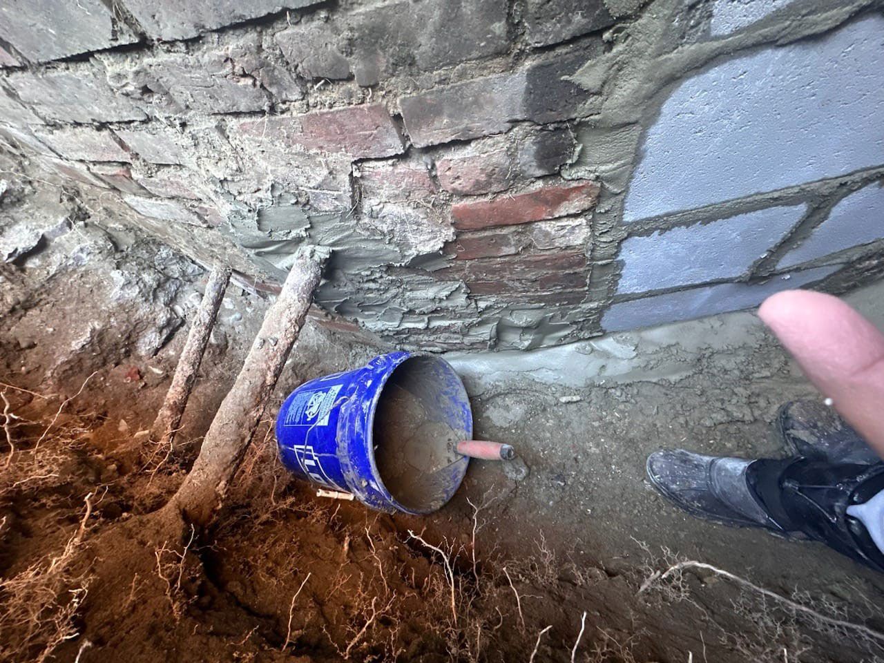 Blue bucket, brick wall and foot in frame.