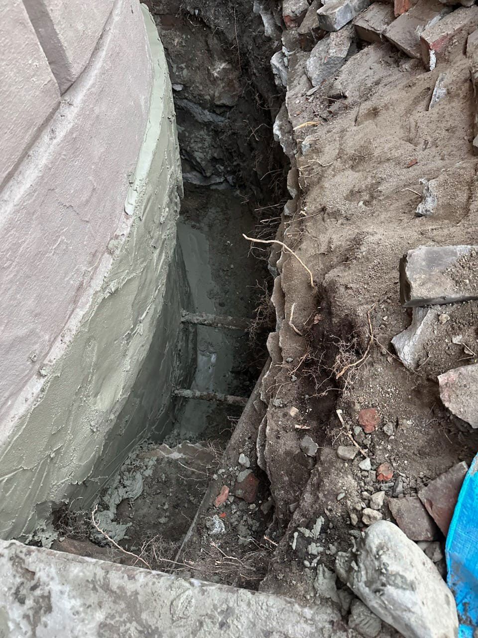 Excavation exposing a concrete structure with a ladder. Gray concrete and soil.