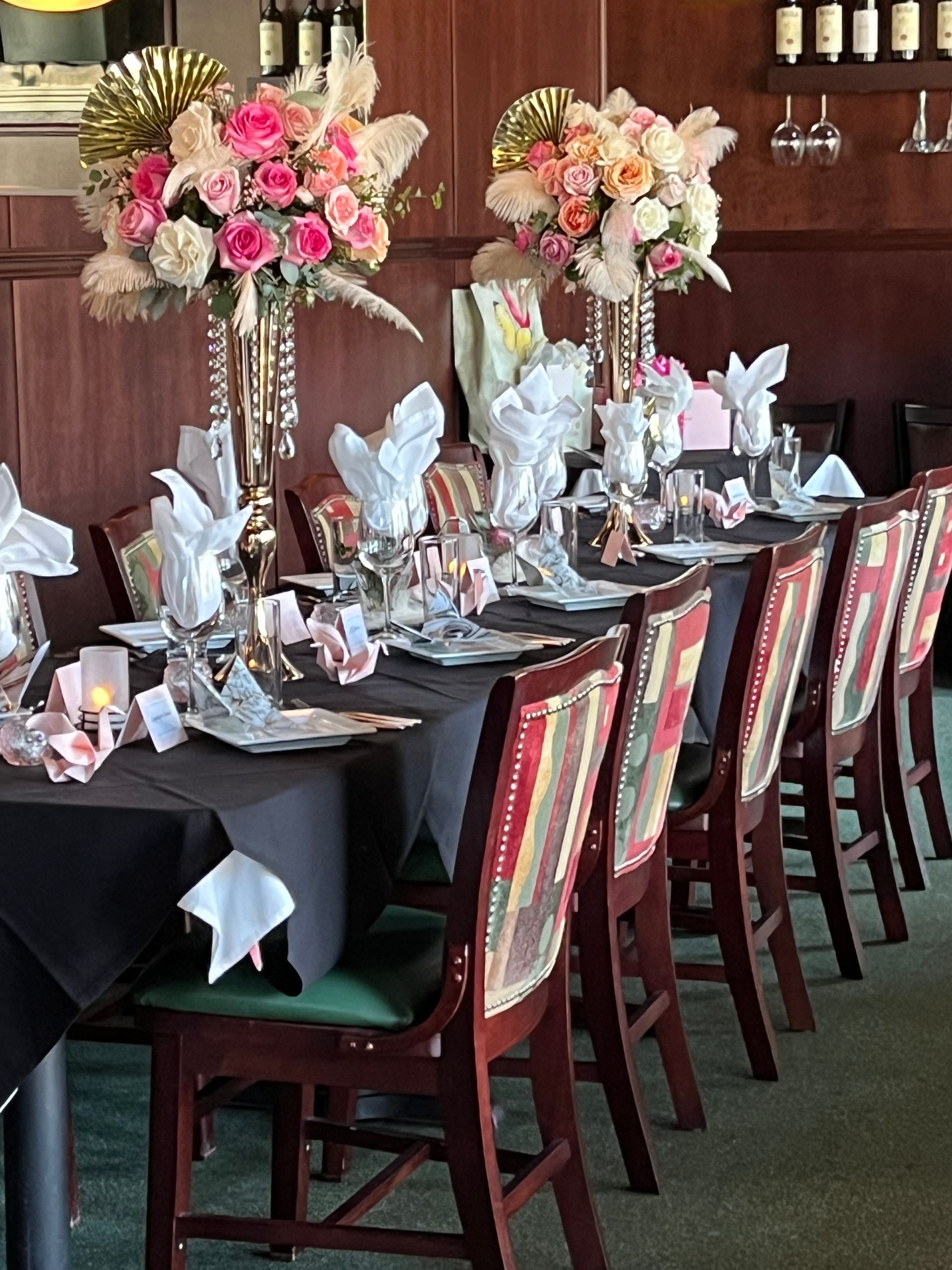 Decorated banquet table with black linens, folded napkins, wine glasses, and pink floral centerpieces in a dining room