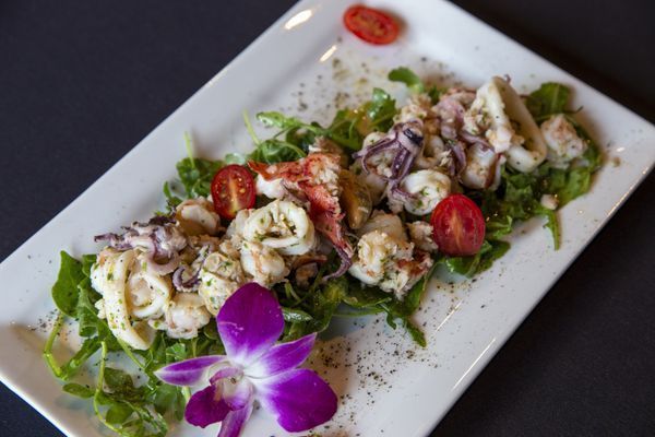 Seafood salad with tomatoes and an orchid flower on a white plate.