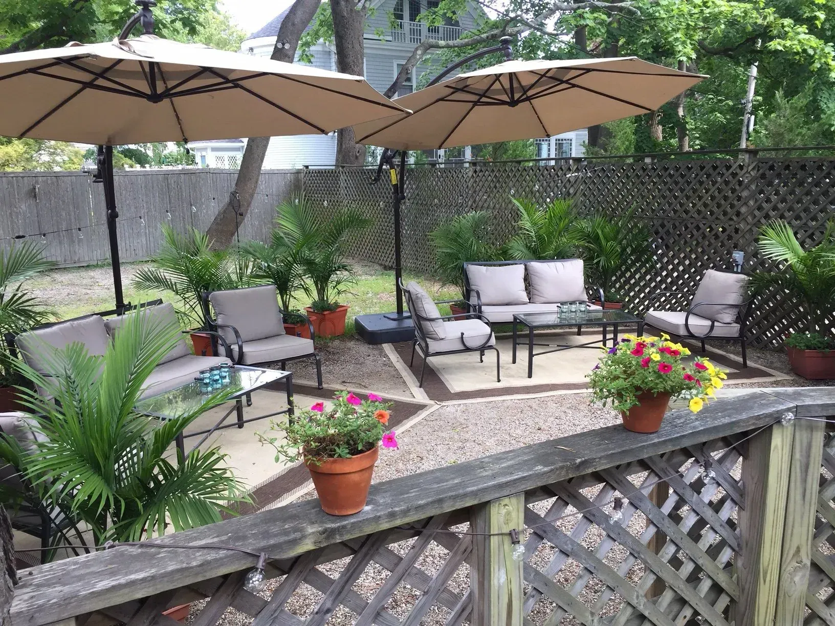 Patio with tan umbrellas, outdoor furniture, potted plants, and a wooden fence.