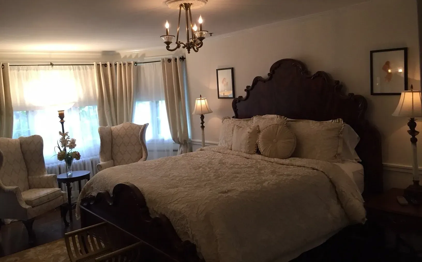 Elegant bedroom with a large bed, chairs, and window, decorated in neutral colors.