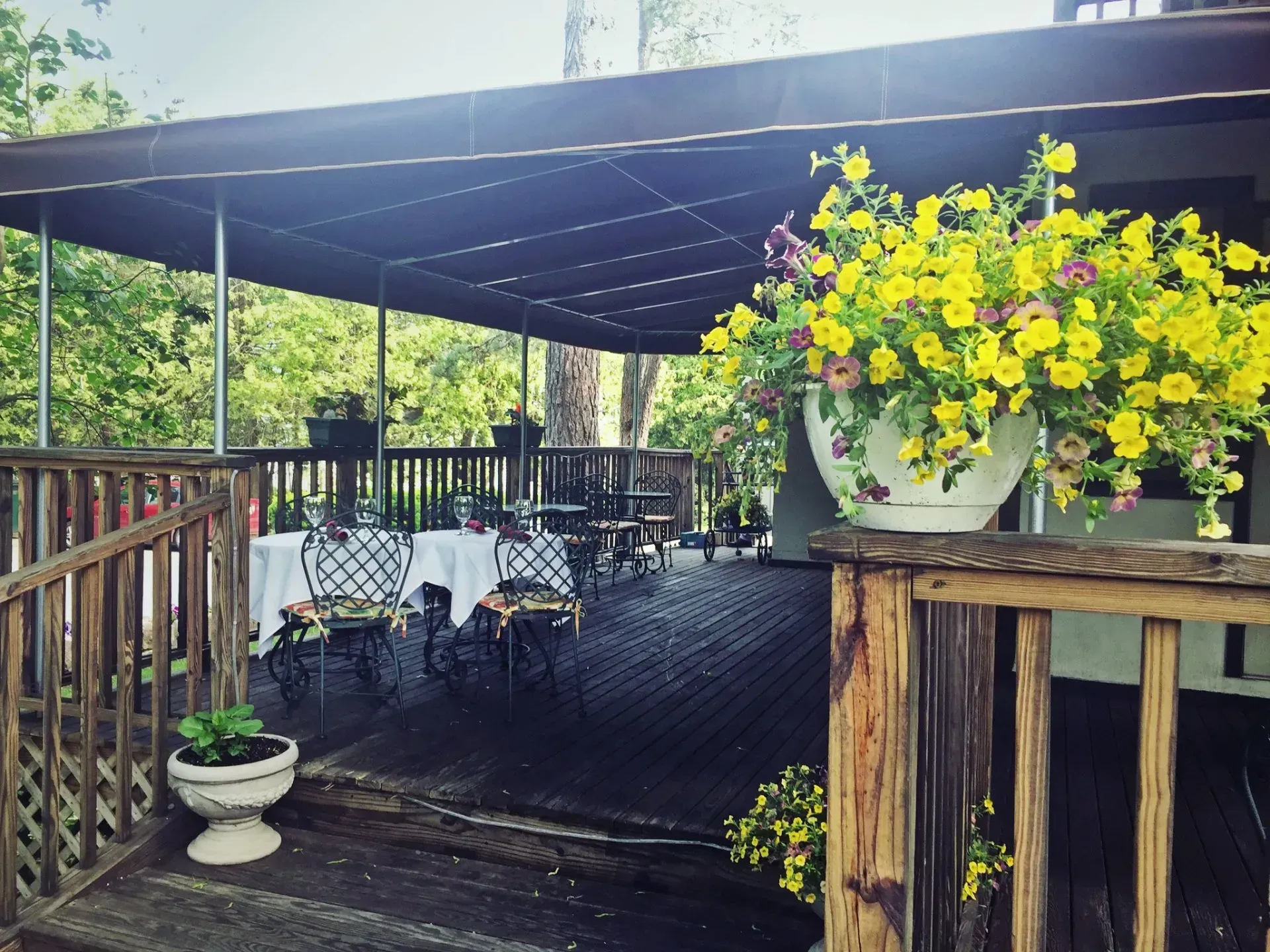 Patio with tables set for dining, yellow flowers in hanging baskets, wooden deck.