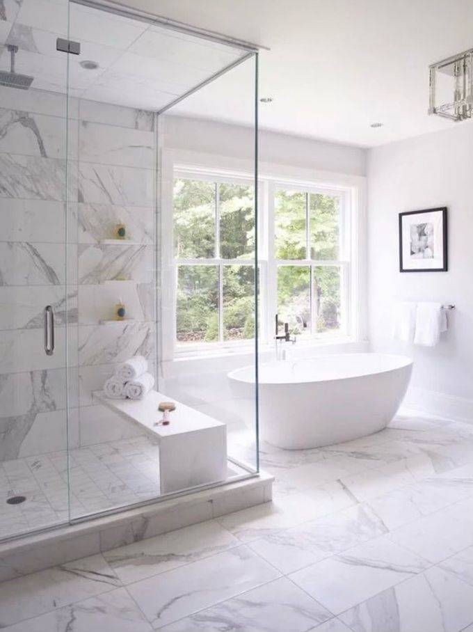 Luxurious white marble bathroom with a glass shower, freestanding tub, and bright windows.