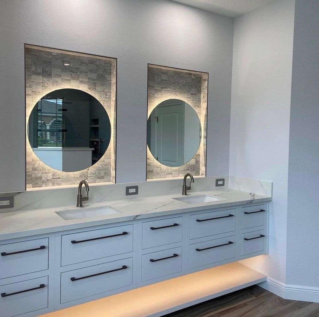 Two mirrors with circular lights above a double vanity in a bathroom.