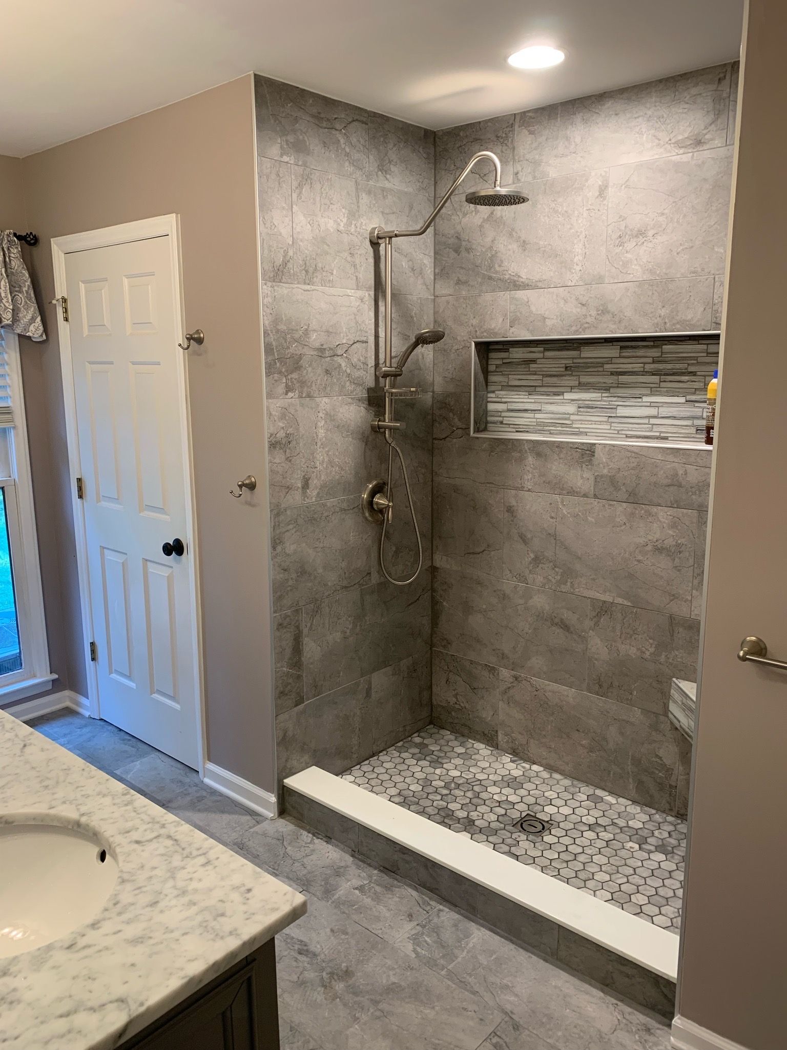 Bathroom remodel with gray tiled shower and pebble floor, built-in niche.