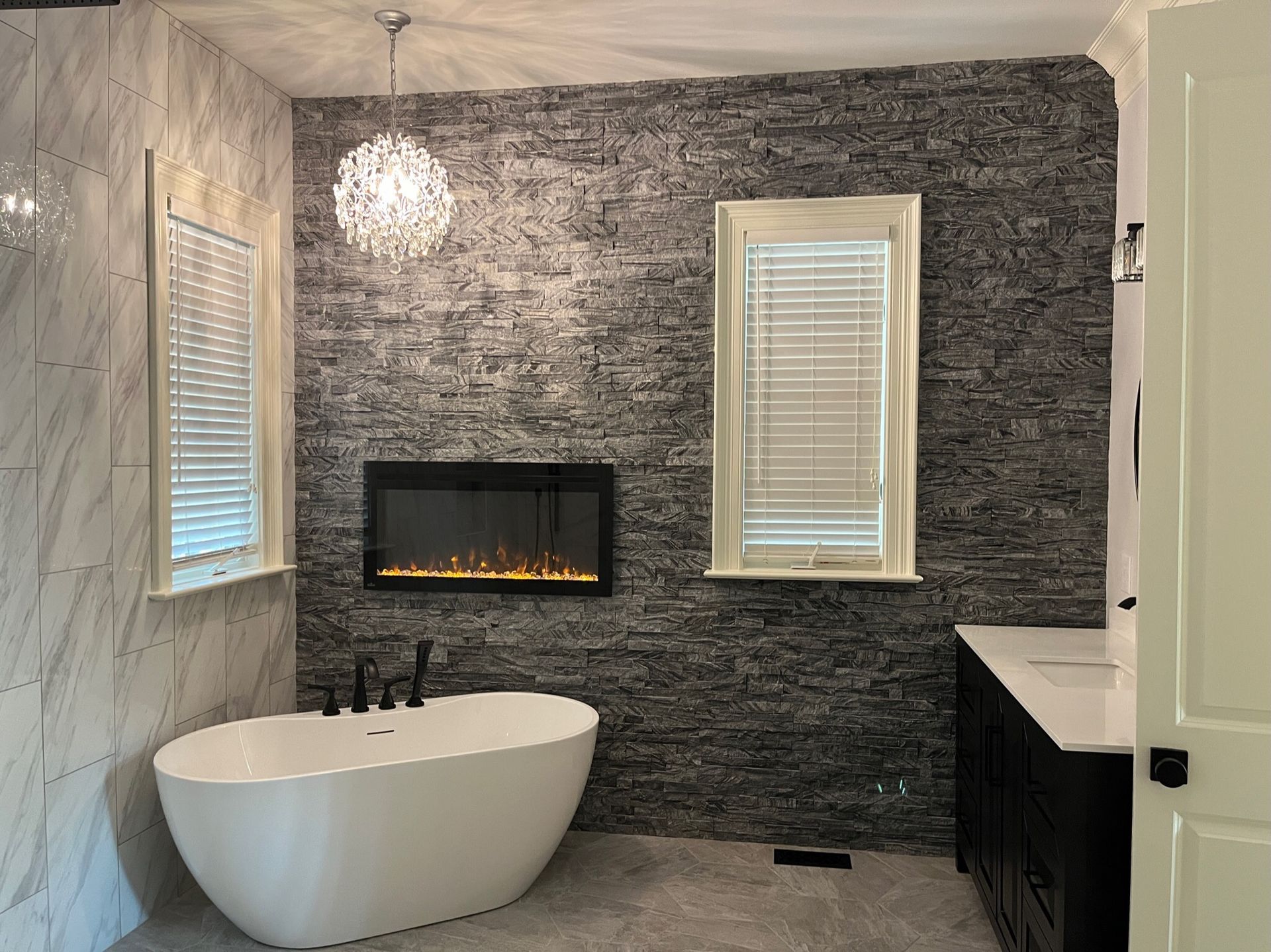 Modern bathroom with a freestanding tub, fireplace, and textured stone wall.