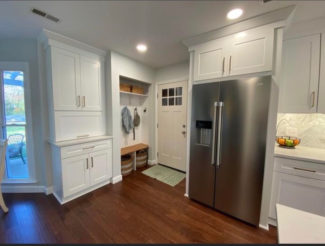 White kitchen with a stainless steel fridge, dark wood floors, and a door leading outside.