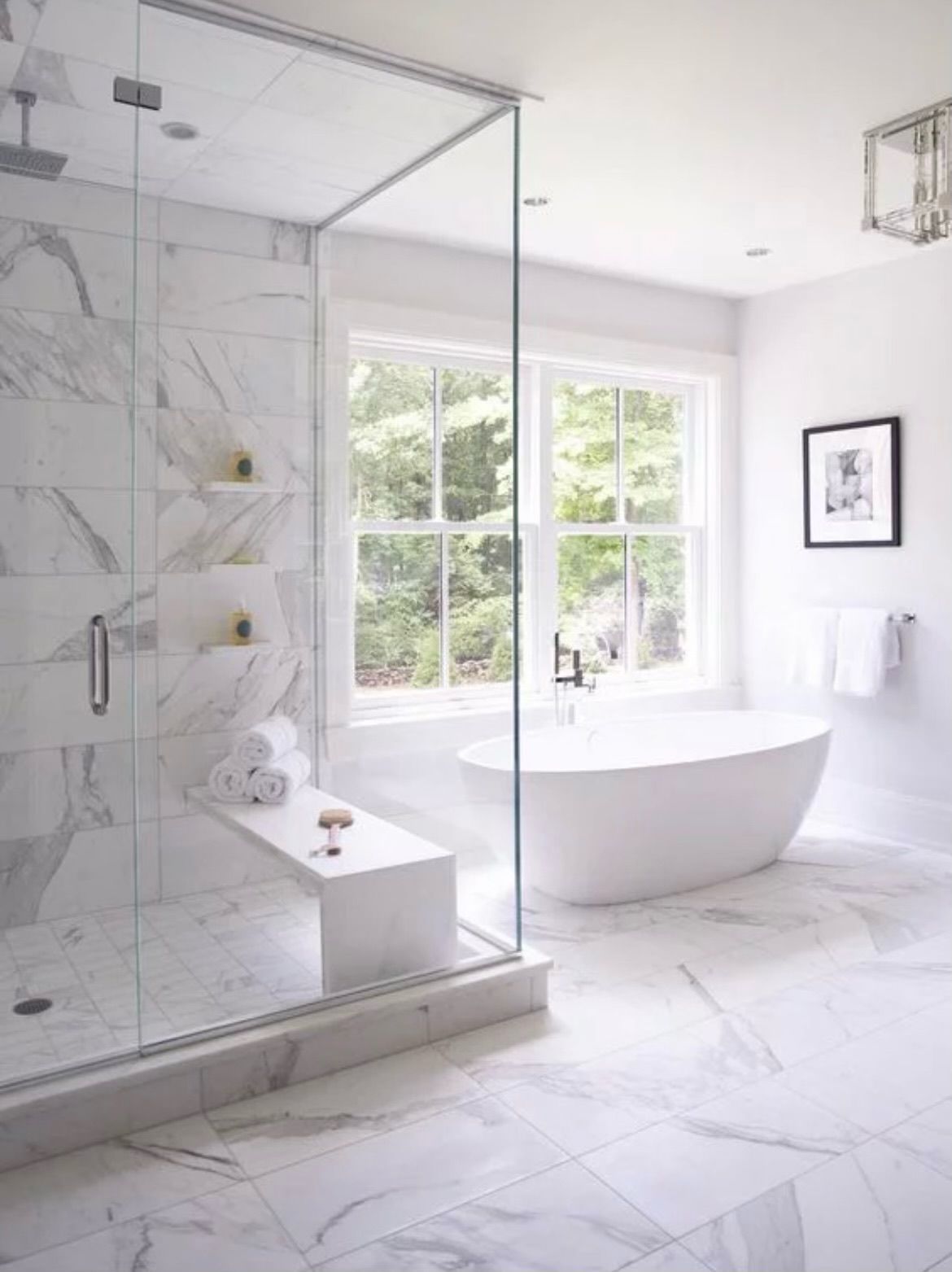 Elegant white marble bathroom with a glass shower, soaking tub, and large window.