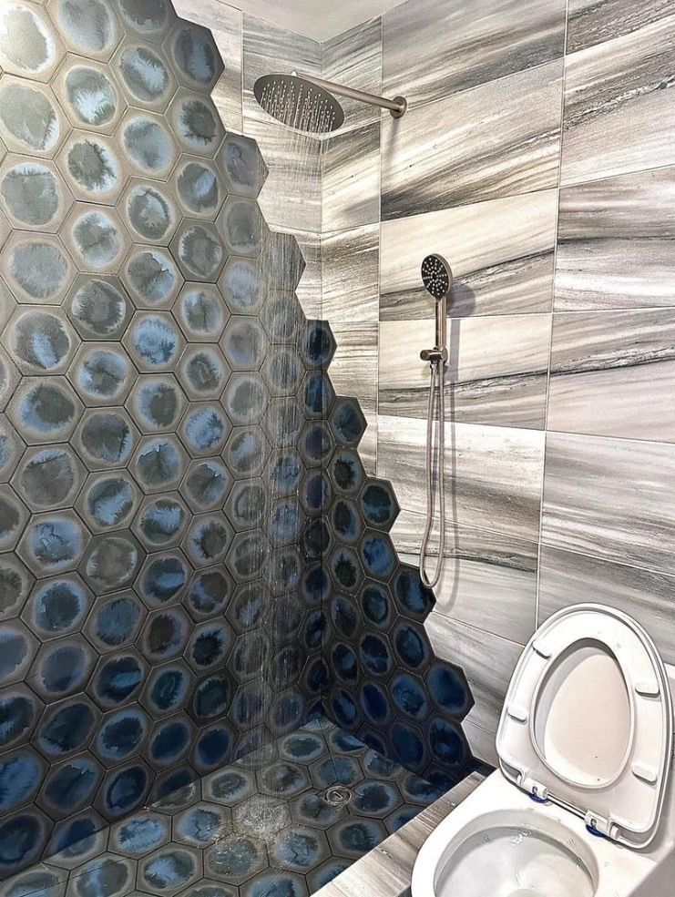 Shower with blue stone tile wall and gray marble walls, toilet in foreground.