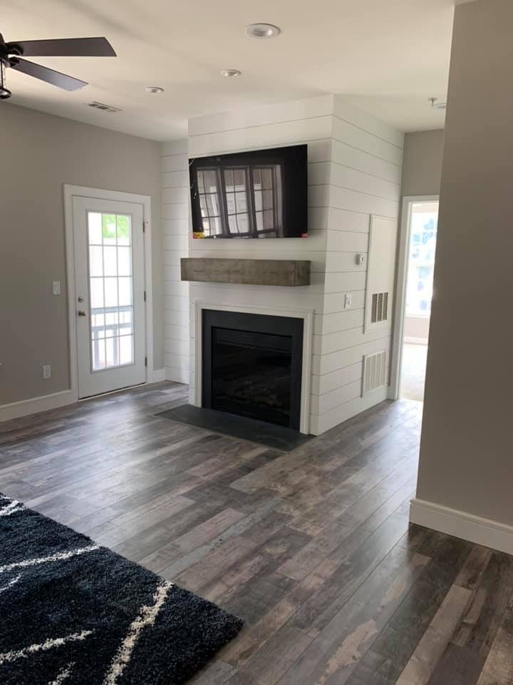Living room with fireplace and TV. Gray wood floors and walls, white door and trim.