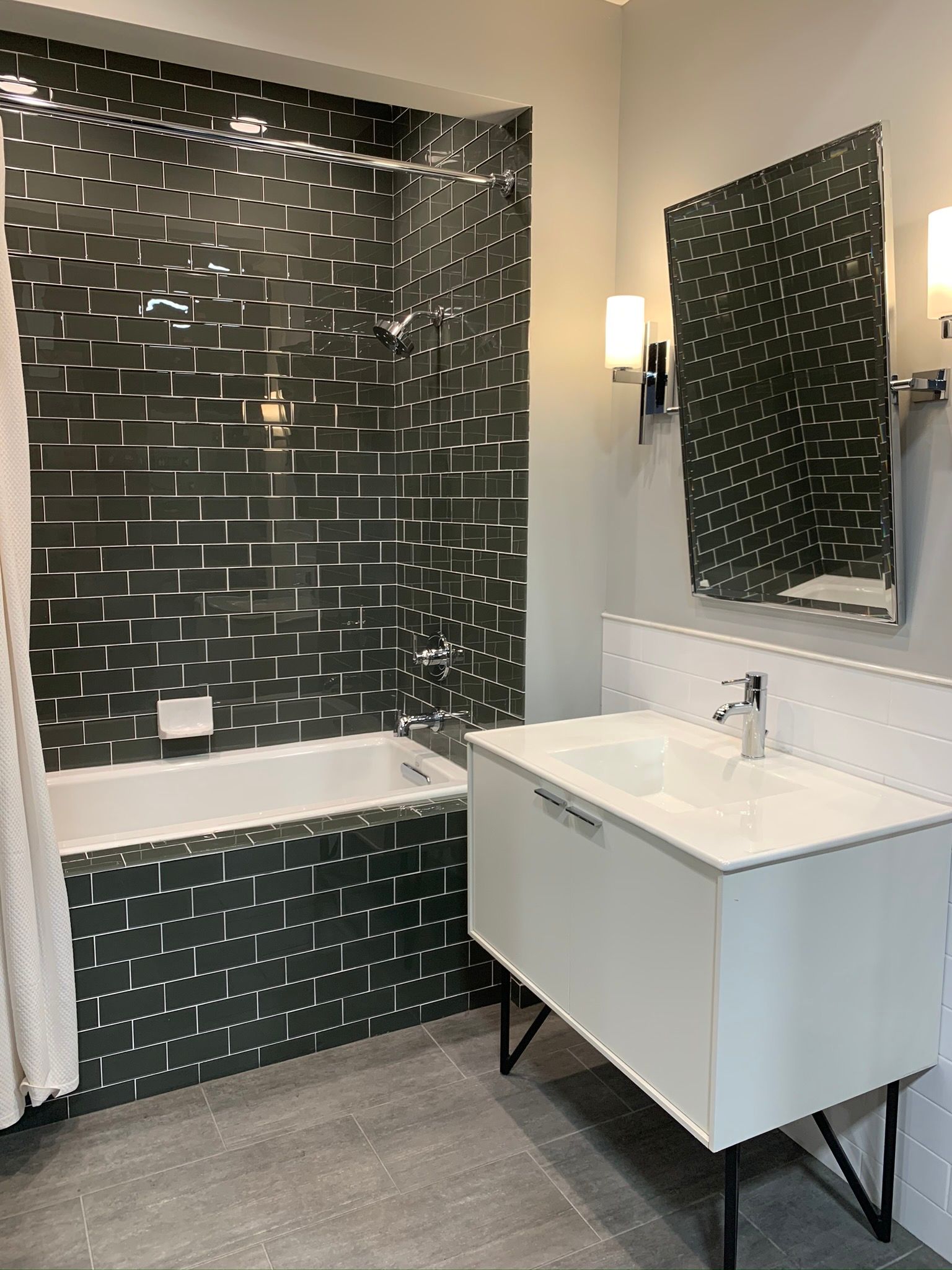 Modern bathroom with dark green tiled shower, white vanity, and a large mirror.