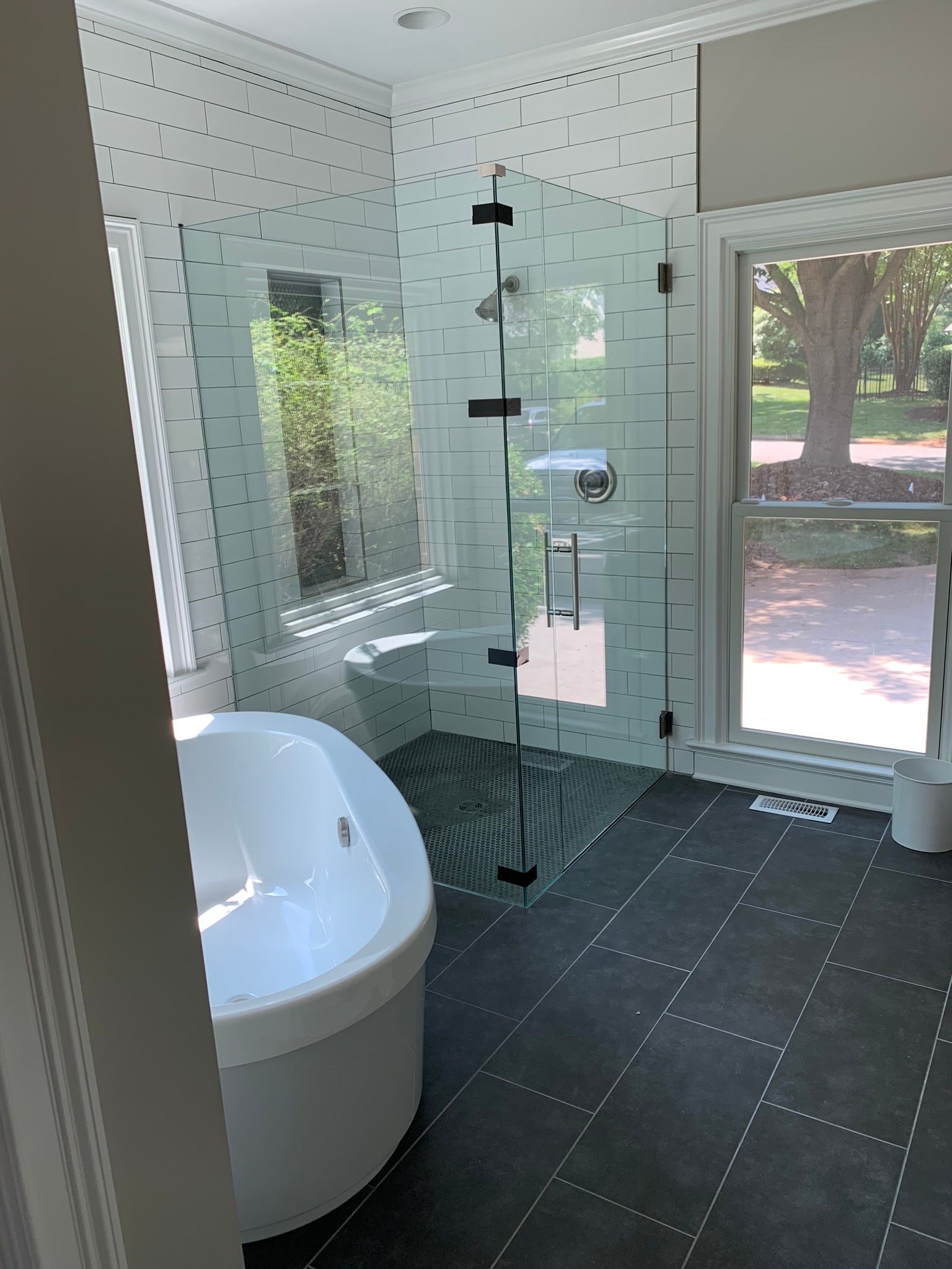 Bathroom with a glass shower, soaking tub, and dark tiled floor.