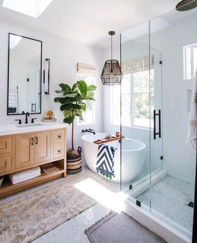Spacious white bathroom with a freestanding tub, glass shower, wooden vanity, and large mirror.
