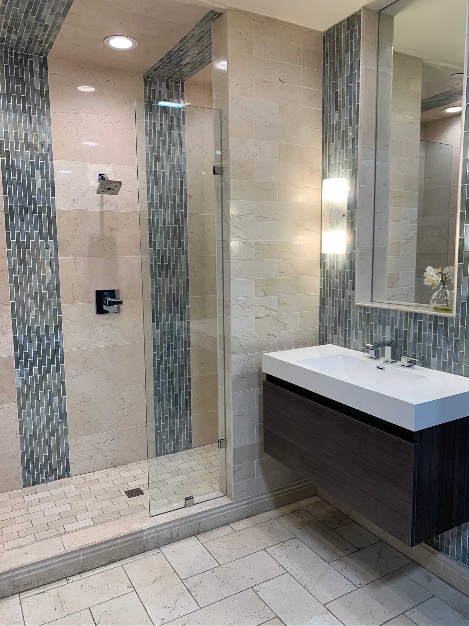 Modern bathroom with glass shower, floating vanity, and stone tiles.