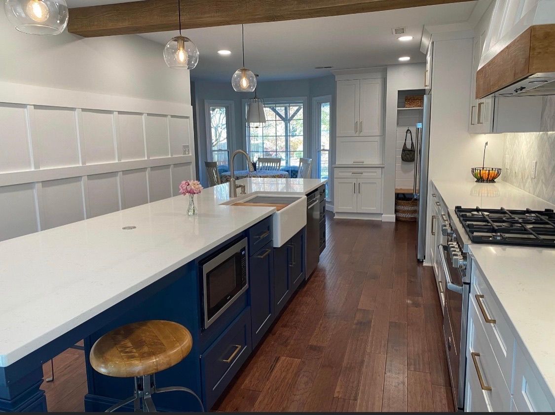 Modern kitchen with navy blue island, white countertops, and hardwood floors.
