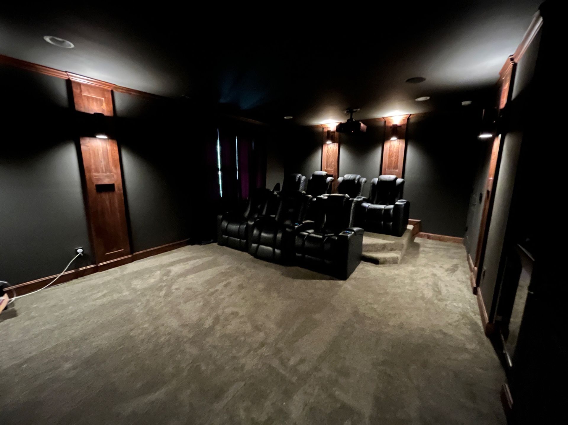 Home theater room with black leather seating, dark walls, and carpet.