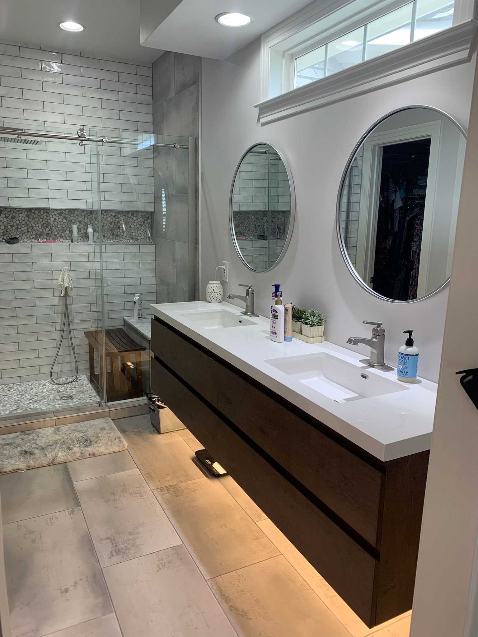 Modern bathroom with double vanity, round mirrors, and a walk-in shower with textured tiles.