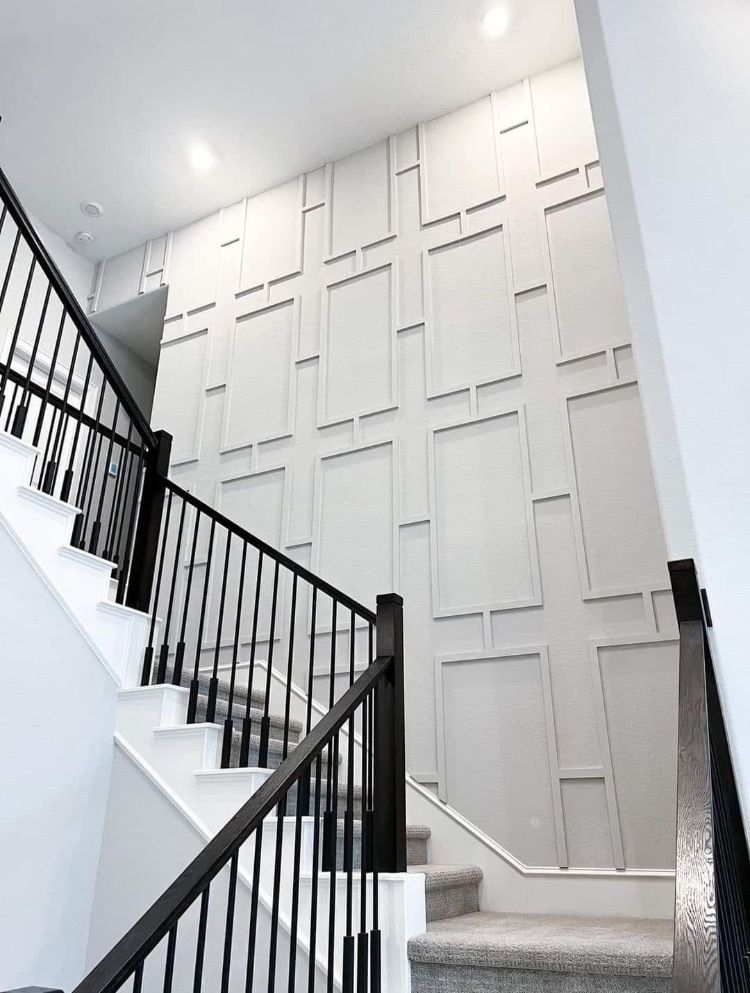 Staircase with white steps, black railing, and textured gray wall with geometric design.