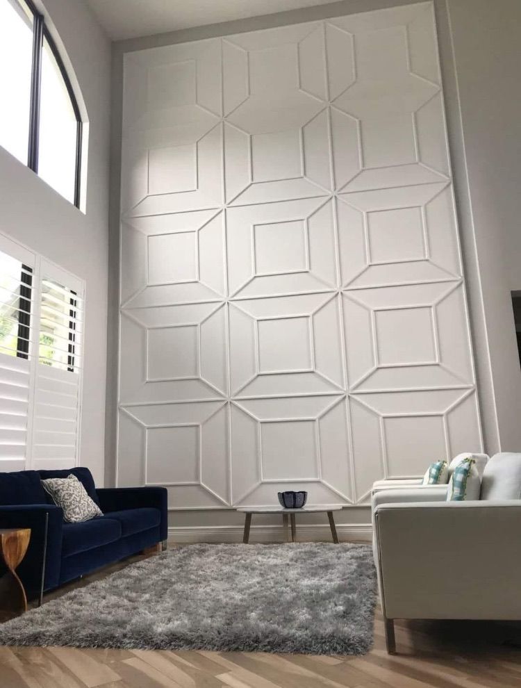 White geometric wall decor in a modern living room with a blue couch, two white chairs, and a grey rug.