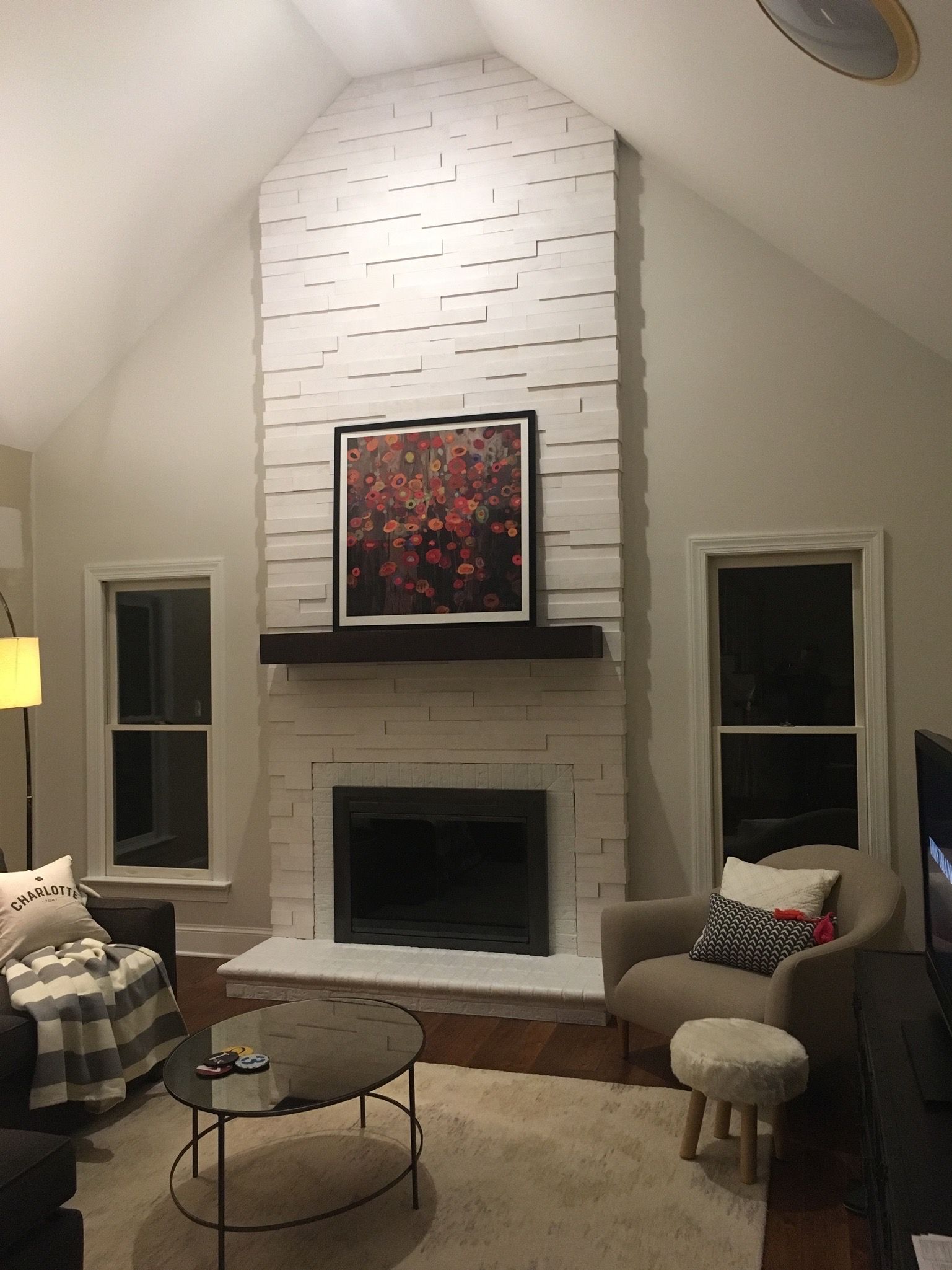 A living room with white brick fireplace, dark artwork, two windows, and cozy seating.