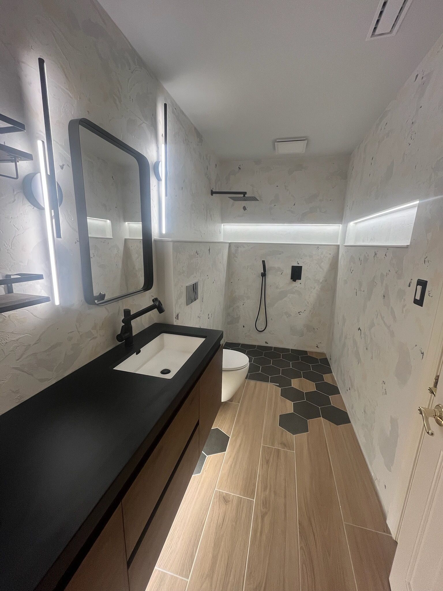 Modern bathroom with wood floor, concrete walls, black fixtures, and a long vanity.