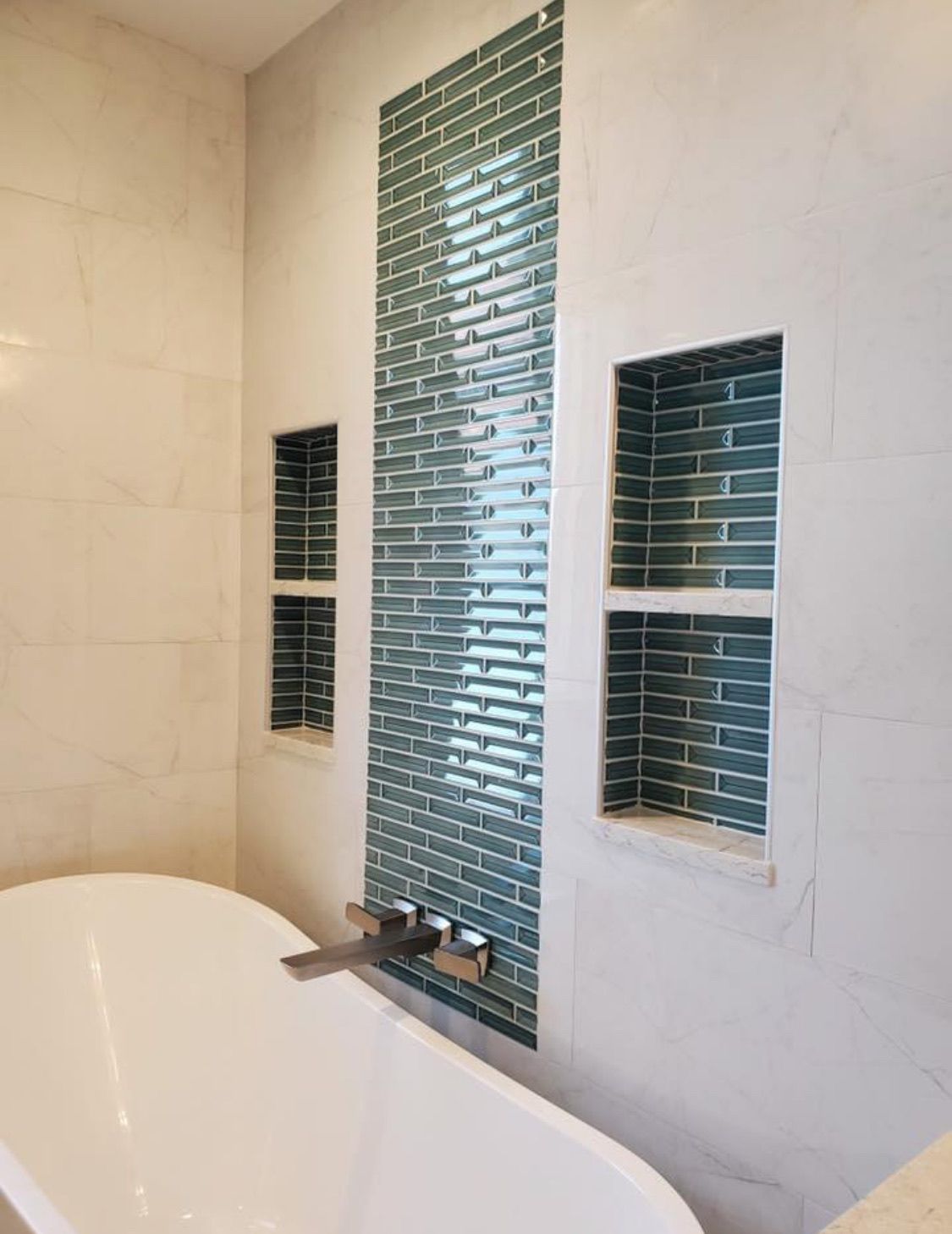 A white bathtub with built-in blue tile accents and two niches in a bathroom.