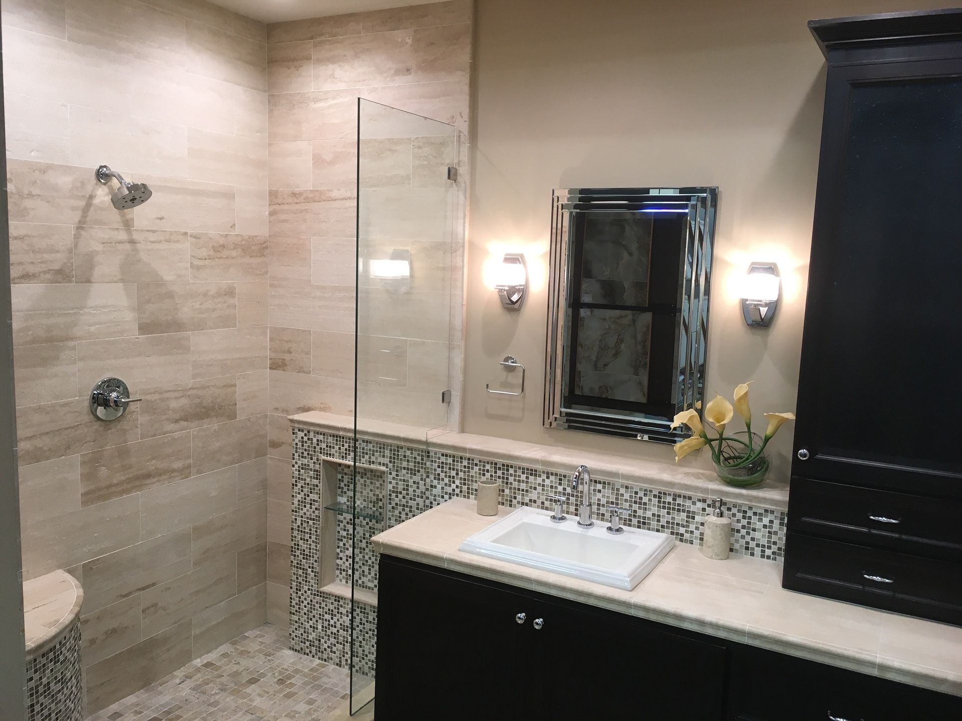 Modern bathroom with a glass shower, dark cabinets, and light-colored tile.