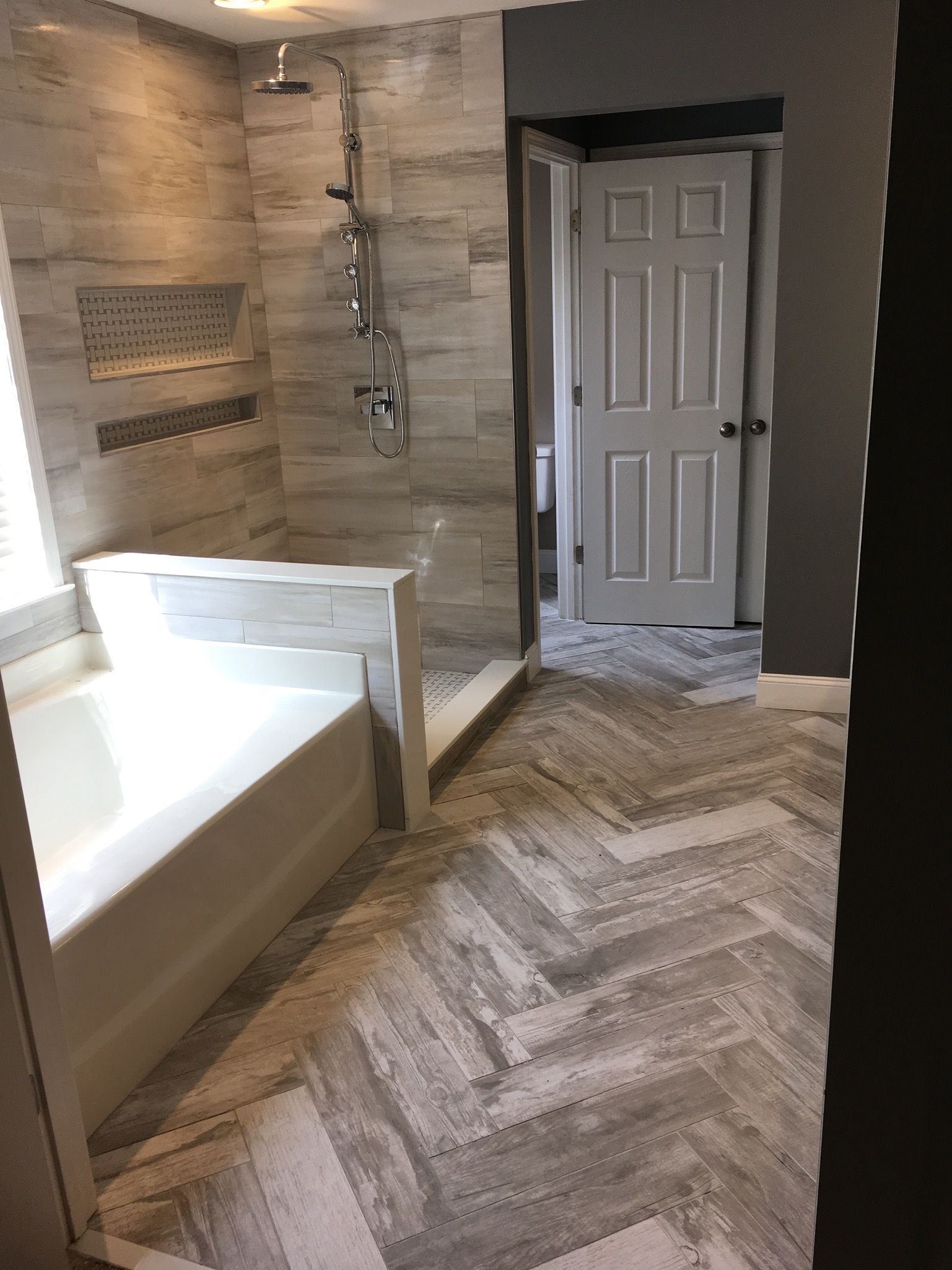Bathroom with light gray herringbone tile floor, walk-in shower, and white tub.