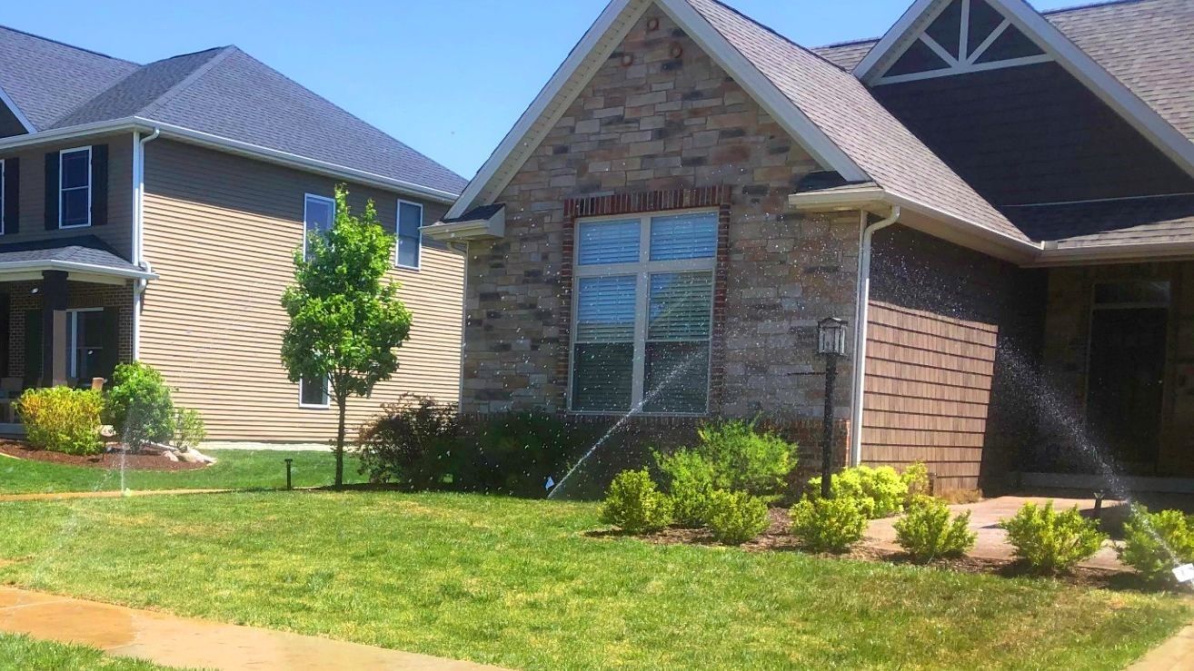A brick house with a gray roof sits next to a tan house
