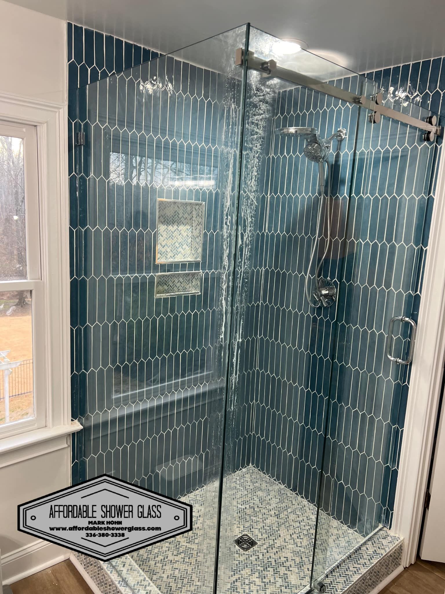 A bathroom with blue tiles and a walk in shower with a glass door.